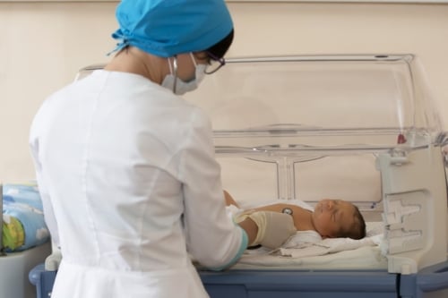 Neonatologist performs health checks on a baby in an incubator
