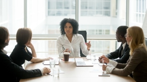 Woman sitting at the meeting table and engaging in conversation with colleagues